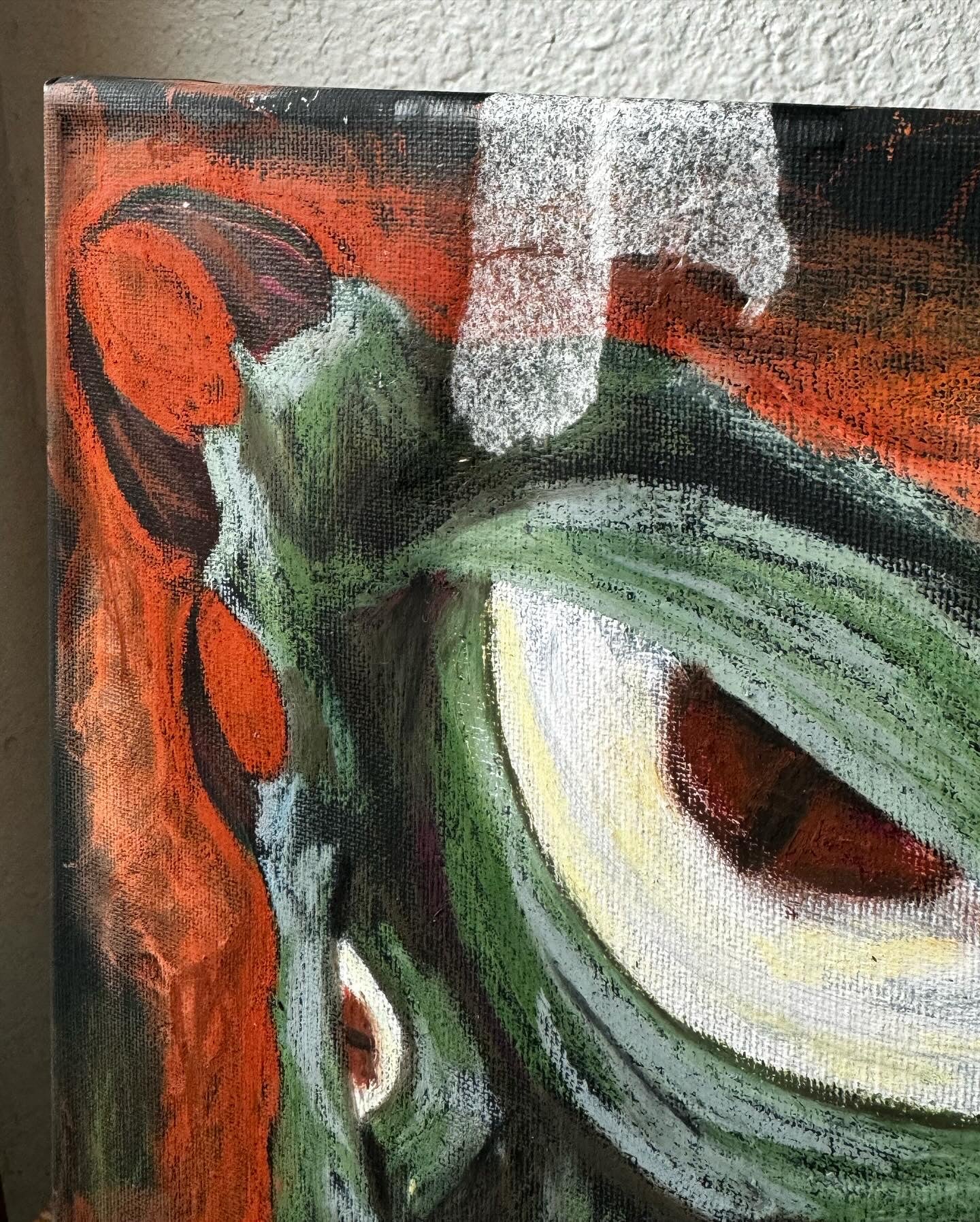 Close up corner picture of an art piece on an easel, green fantastical monster with horns, yellow teeth, and a very large eye. bckground is black and orange, almost entirely oil pastel.
