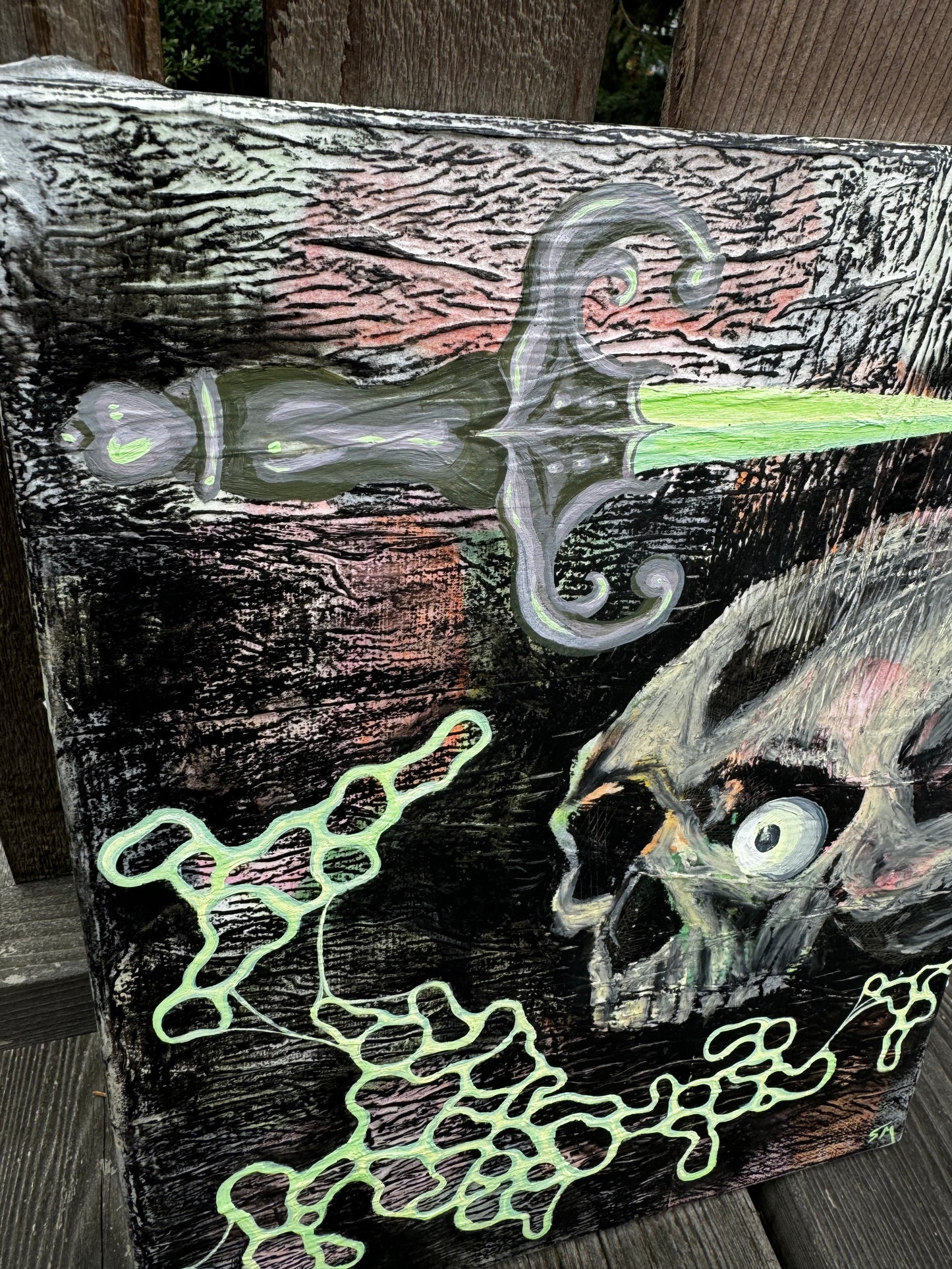 Close up shot of dagger from pastel pink, green, yellow, orange, and black painting. There is wrinkly texture, a skull with an eyeball, a dagger, and circular blobs