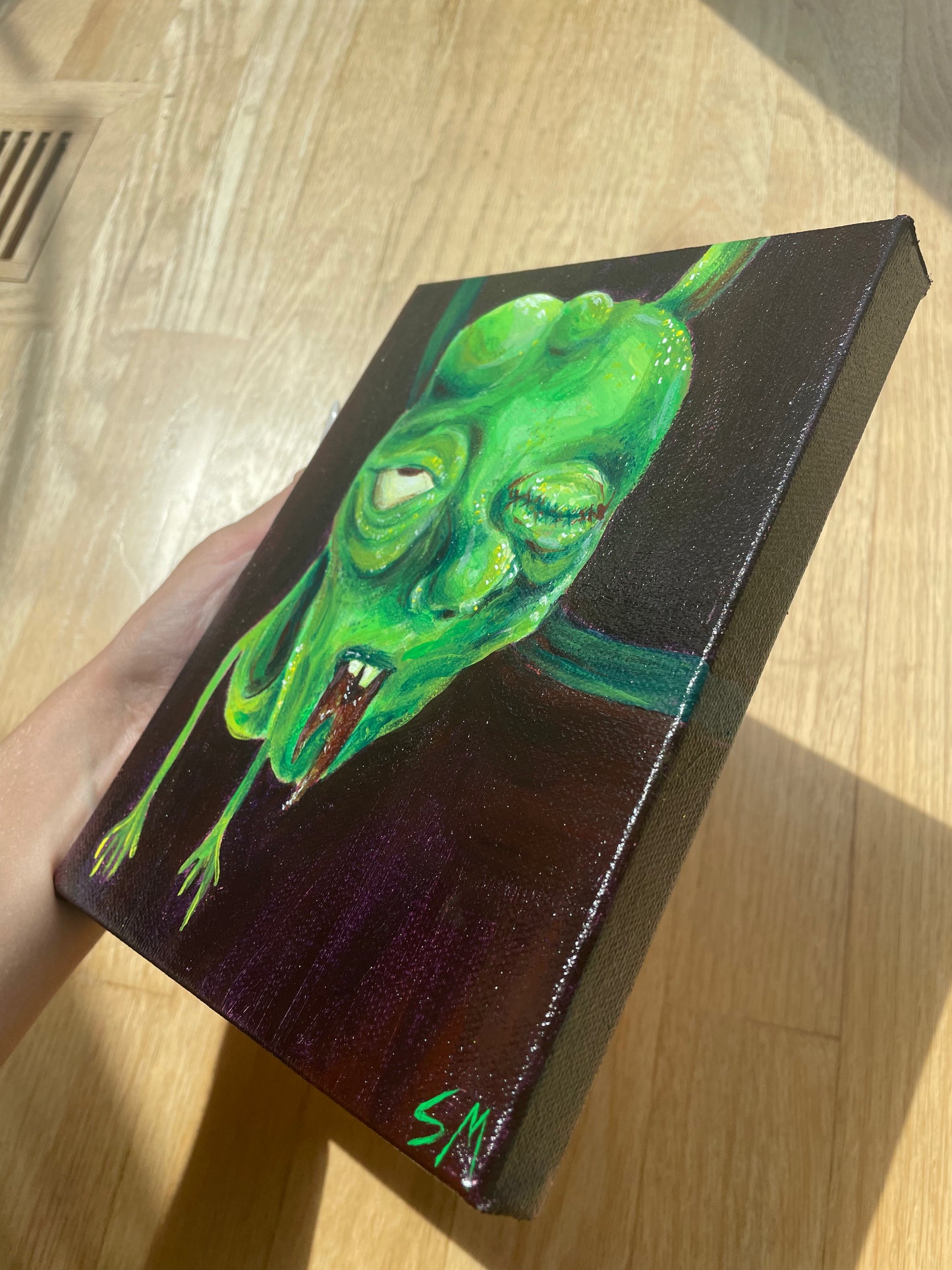 Angle view of an original acrylic painting of a green monster dude by T00thFaerie Art on a 6” by 8” canvas. Painting features a green monster alien hanging down from above. The background is a very dark purple with some hints of brown as well.