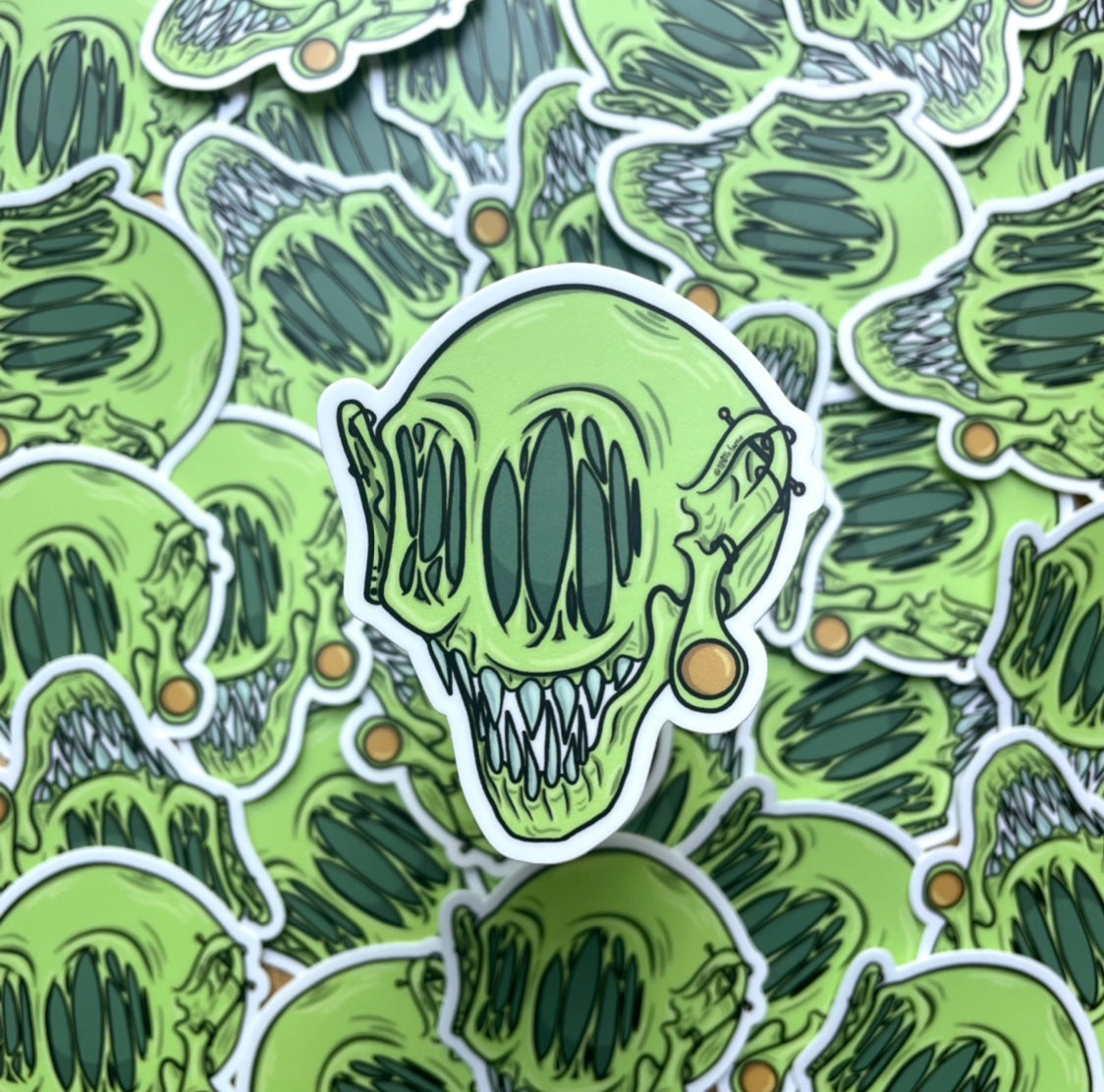 Green whimsical monster head sticker, cartoon style art, mythical creature with gauges and piercings. pile of stickers, product photo