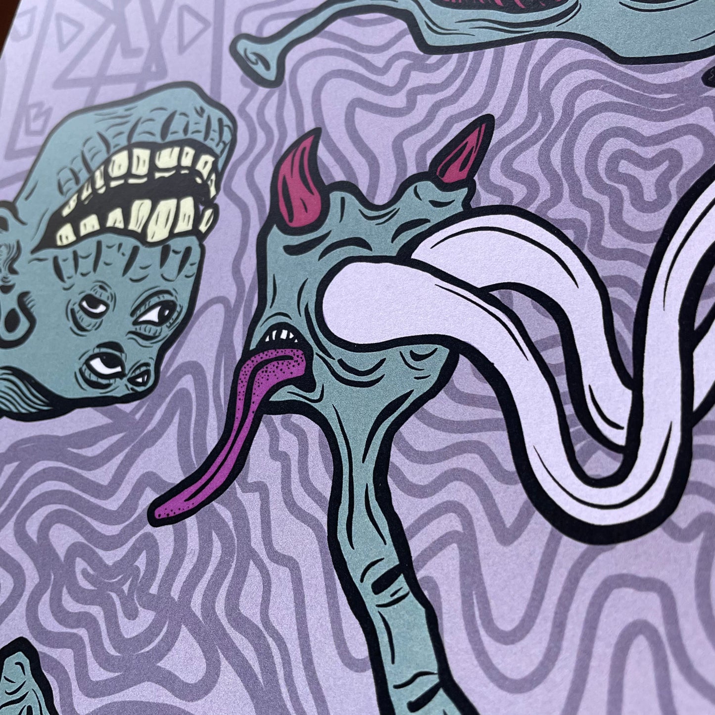 Close up shot of a poster print. Print is graphic, digital art style, showing two green hands. one hand holds up a pointer finger, which turns into a monster head. The hand on the right holds up the rock & roll sign (horns) and those fingers turn into other monster heads.