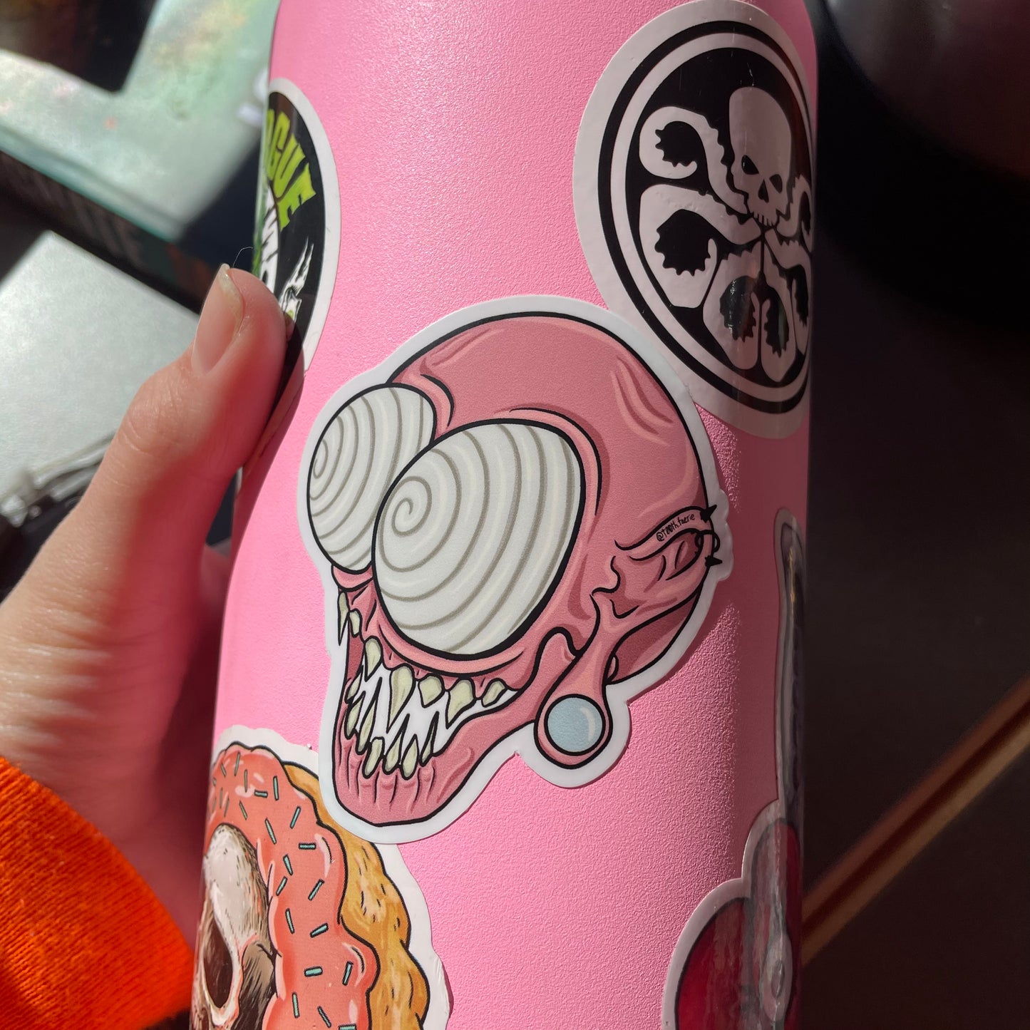 Pink whimsical spooky monster head vinyl sticker, cartoon style art, mythical creature with gauges and piercings. Shown on a bubblegum pink waterbottle with some other stickers