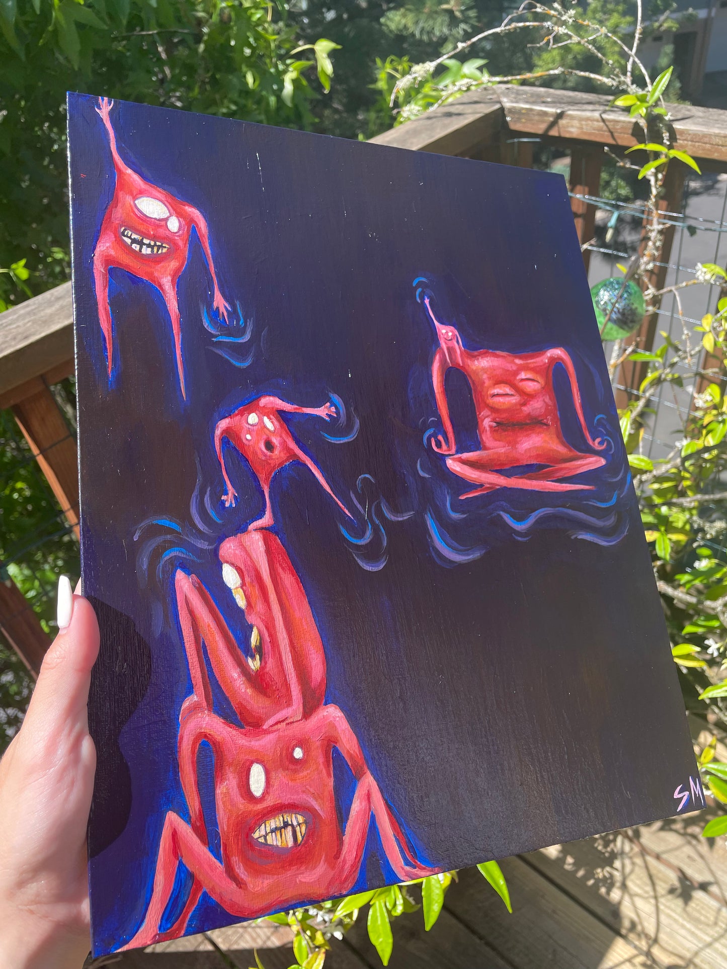 Side angle of a whimsical acrylic painting in front of plants. Painting is of six pinky orange square-shaped monsters/critters/creatures sitting, meditating, hanging, and balancing in space.