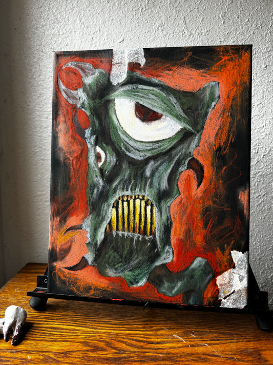 Photo of art piece on an easel, green fantastical monster with horns, yellow teeth, and a very large eye. bckground is black and orange, almost entirely oil pastel. 