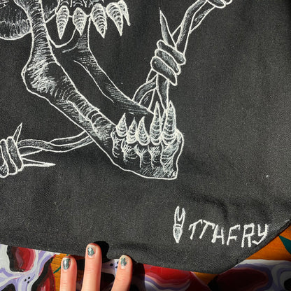 Another detail photo of a black customized tote bag on a wooden painted skull table. Tote bag has a white fabric painted skull with a long jaw on it