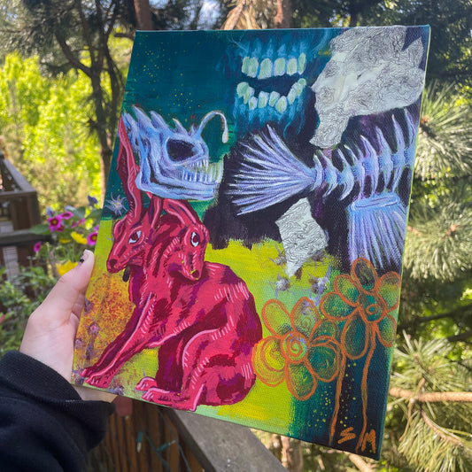 Hand holding a painting. Whimsical, original mixed-media painting, trippy two-headed rabbit artwork, angler fish skeleton, teeth and gums, orange flowers. 
