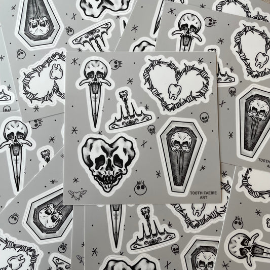 A pile of sticker sheets. Stickers are tattoo flash style featuring a heart-shaped skull, a skull dagger, a tooth crown, a skull coffin, and a barbed wire heart with a tooth in the middle.
