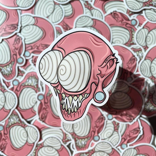 Pink whimsical spooky monster head vinyl sticker, cartoon style art, mythical creature with gauges and piercings. One large sticker in focus over a pile of the same stickers.