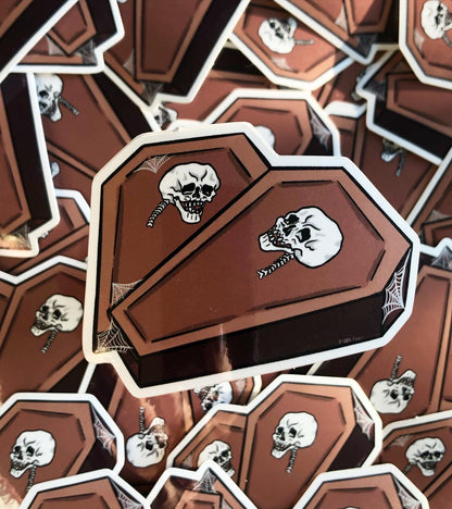 Photo of a vinyl sticker, two coffins in the shape of a heart with a skull on each and some spiderweb detailing