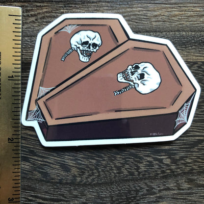 ruler showing height of a vinyl sticker of two coffins in the shape of a heart with a skull on each and some spiderweb detailing