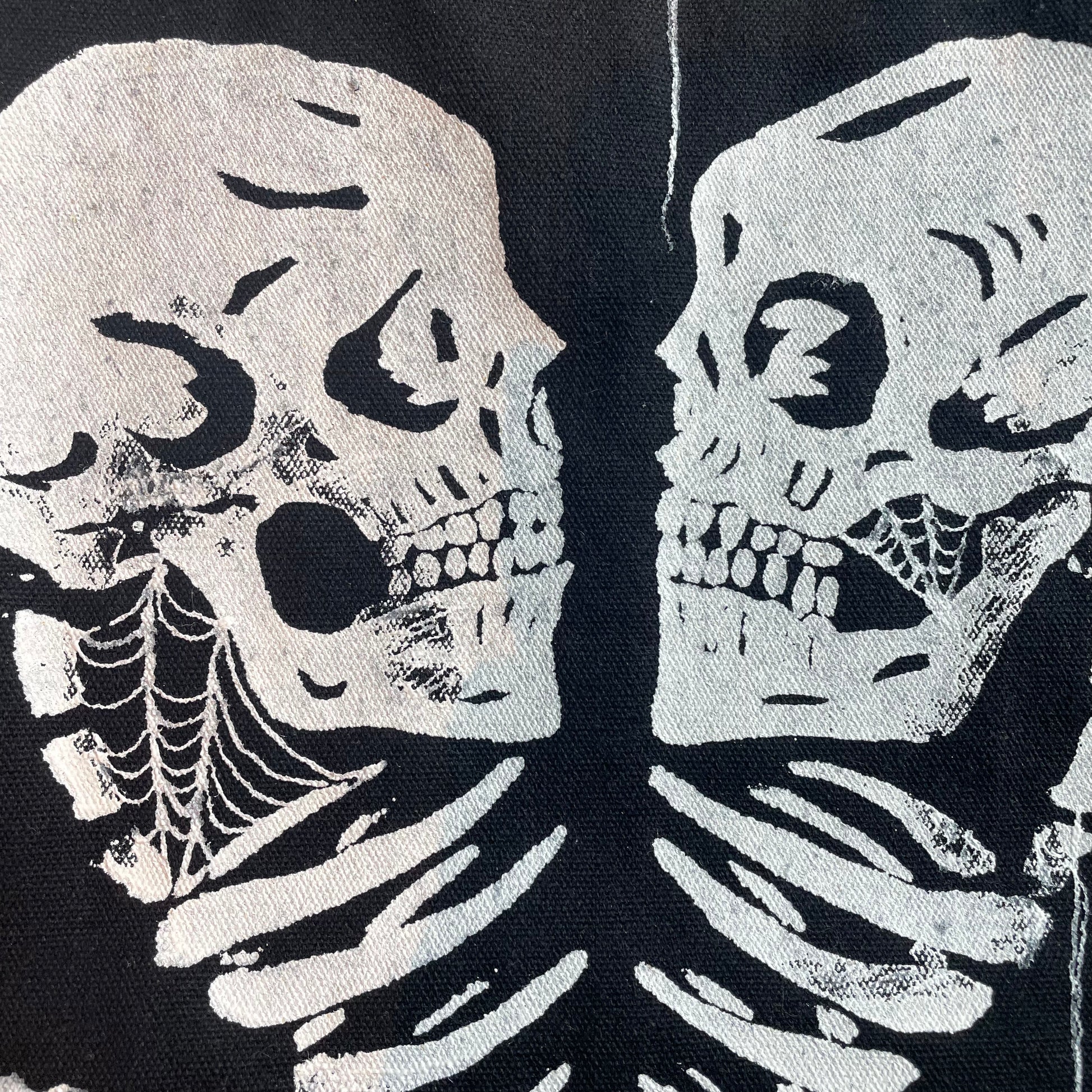 Close up shot of two screen-printed skulls arranged in a heart on a custom black tote bag